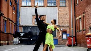 Oskar Odiakosa in a black top and trousers and Lauren Claydon in a lime dress pose outside in Blackpool's Dance Fever.