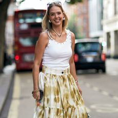 fashion week attendee wearing white studded tank top, tie-dye skirt, sunglasses and silver jewelry, 