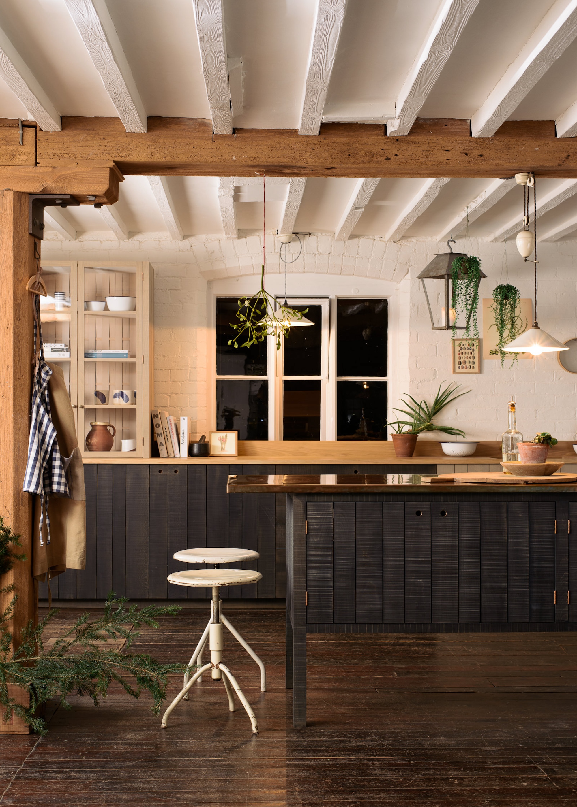 A sawn timber kitchen with dark oak cabinets in a farmhouse-like kitchen. There is also a table with bar stools beside it.