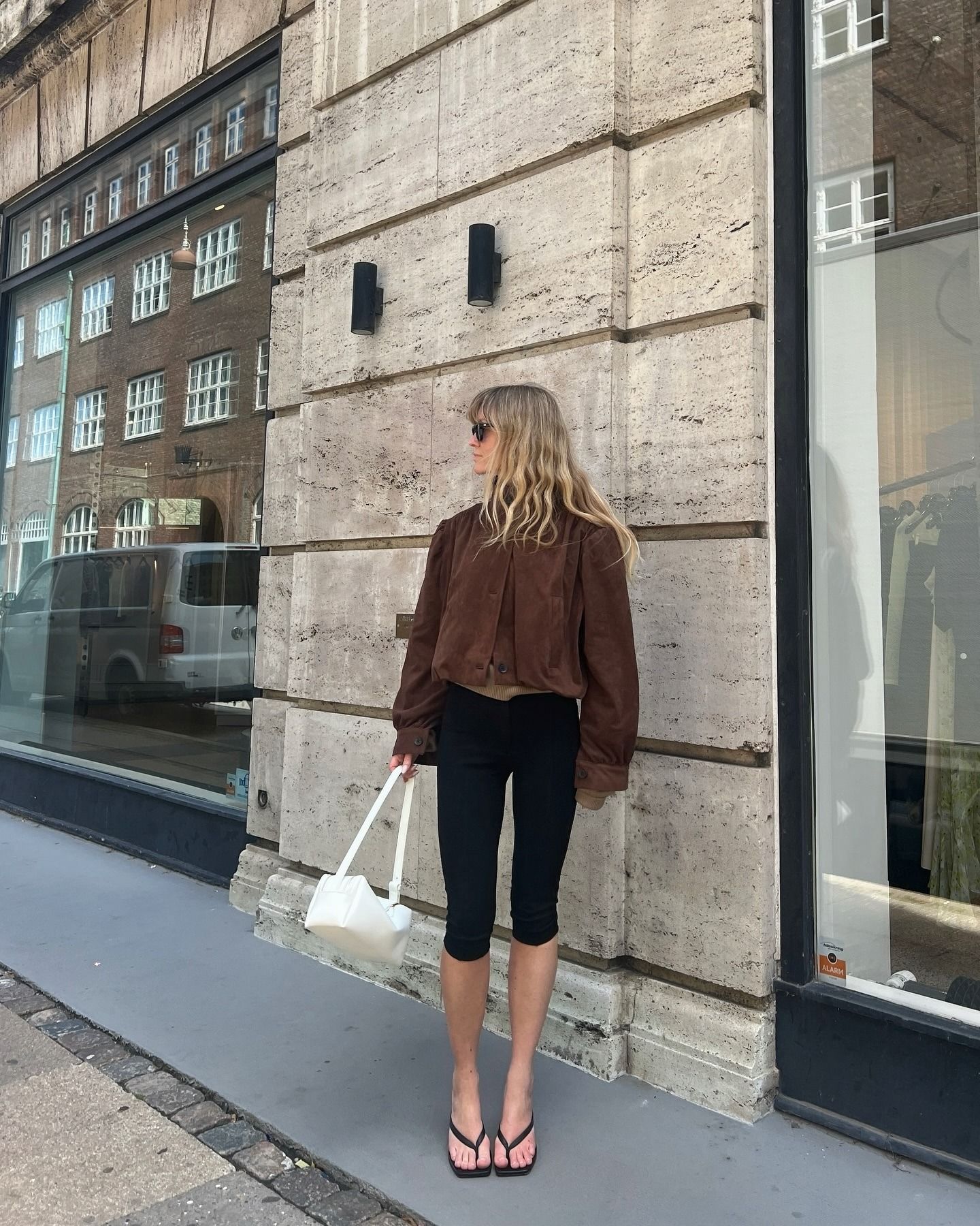 European influencer wearing a brown suede jacket, capri pants, and kitten heel flip-flops