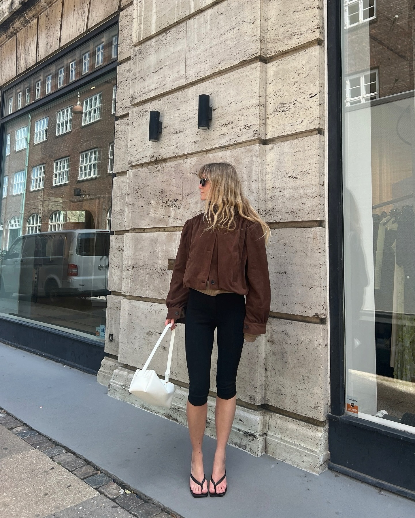 European influencer wearing a brown suede jacket, capri pants, and kitten heel flip-flops