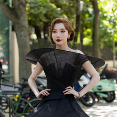 Summerween Gothic Glam Makeup Beauty: Dai Yanni wears a sculptural black mini dress featuring exaggerated fan-like shoulder structures, a fitted bodice,
