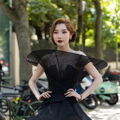 Summerween Gothic Glam Makeup Beauty: Dai Yanni wears a sculptural black mini dress featuring exaggerated fan-like shoulder structures, a fitted bodice,