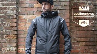Aaron wearing the carbon grey Altura Nightvision Electron jacket, whilst stood in front of a brick wall - image is overlaid with a 'recommends' badge