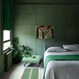 how to make a guest room look more expensive, green colour drenched bedroom with pale grey bedding and carpet, green rug, green throw and stool, artwork, plant