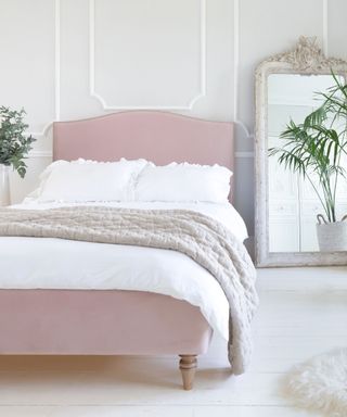 A white bedroom with a pink bed with white bedding, a mirror, and a wall with wall paneling