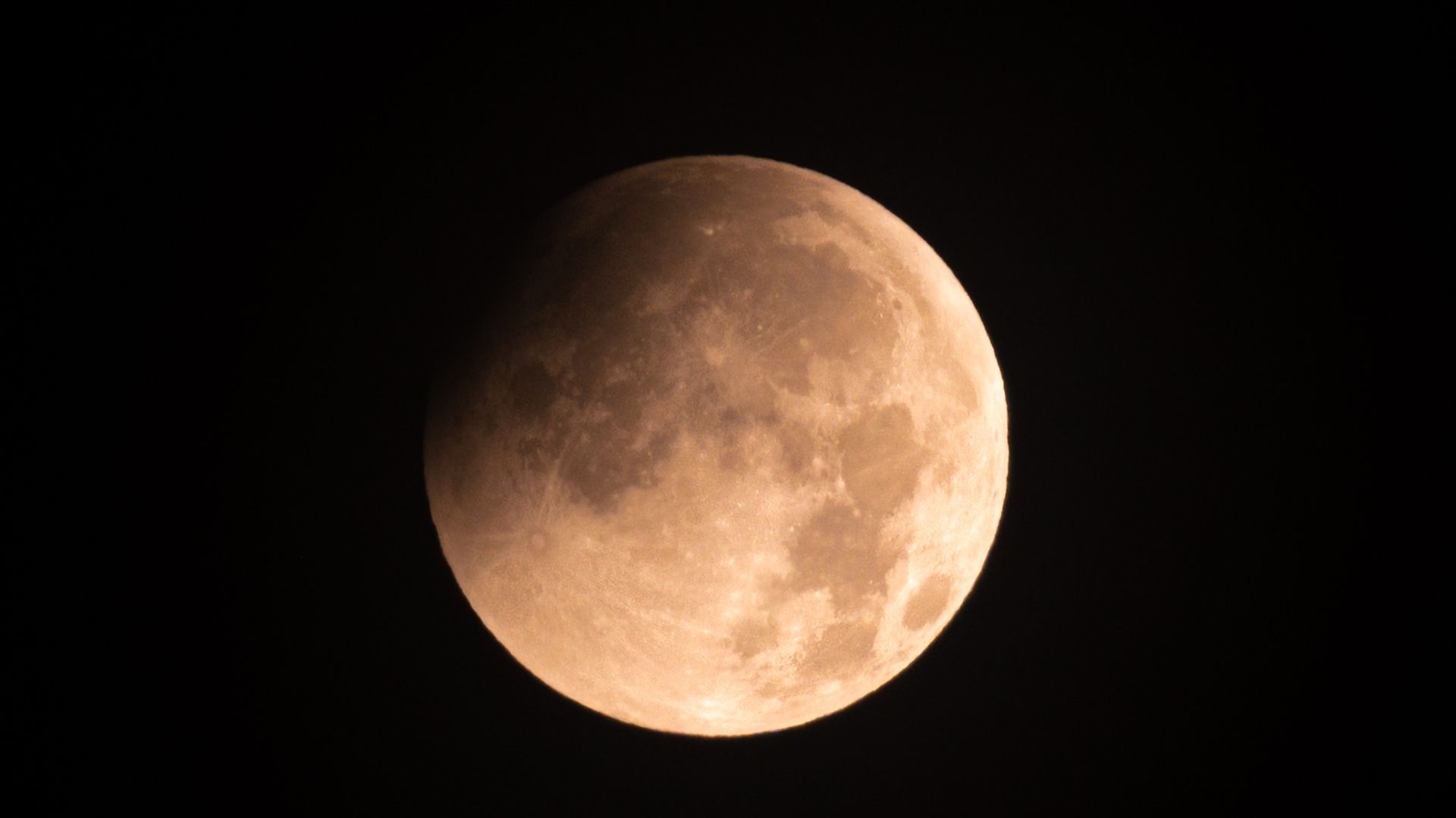 A full moon is photographed in a black sky with its upper left portion shadowed during a lunar eclipse.