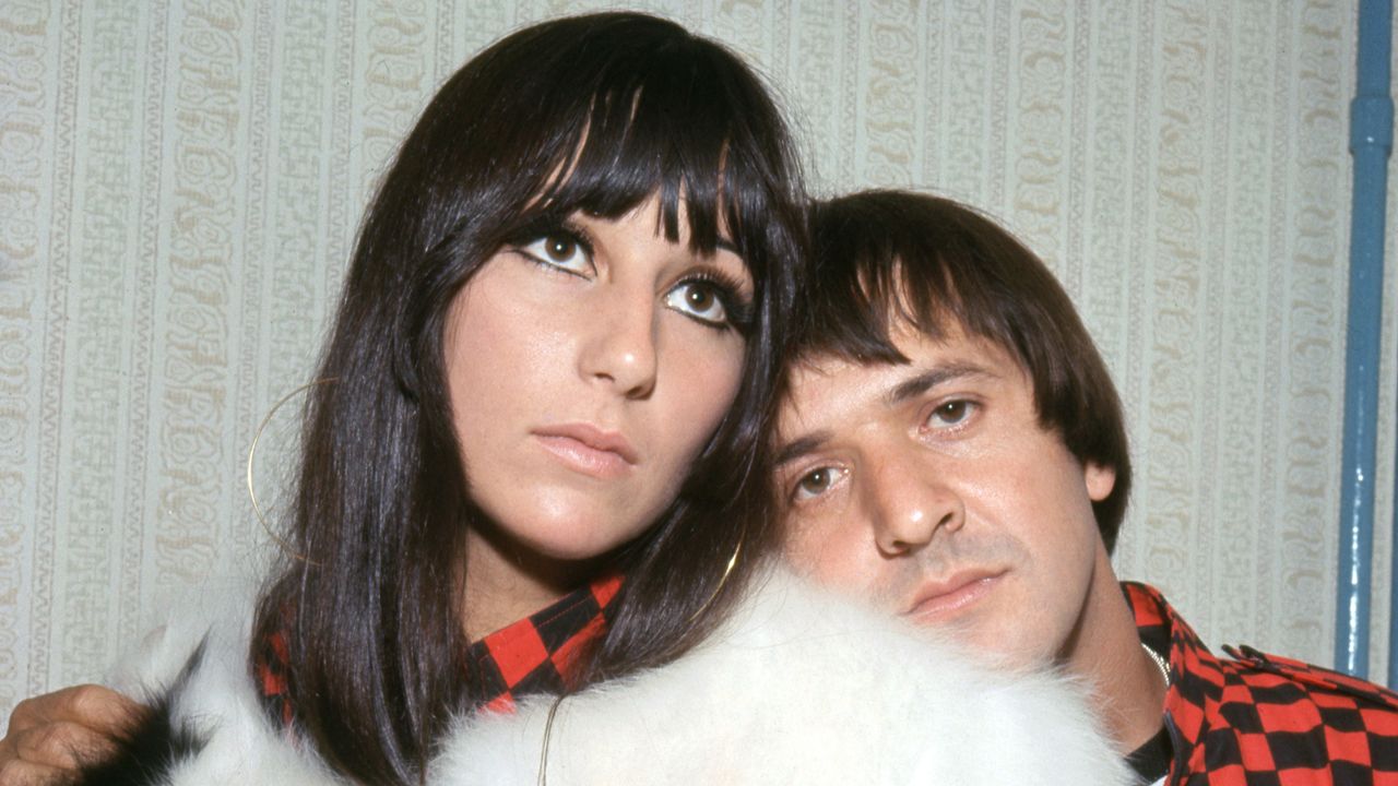 Cher wears a white fur coat while ex-husband Sonny Bono stands behind her wearing a black and red checked shirt in 1966