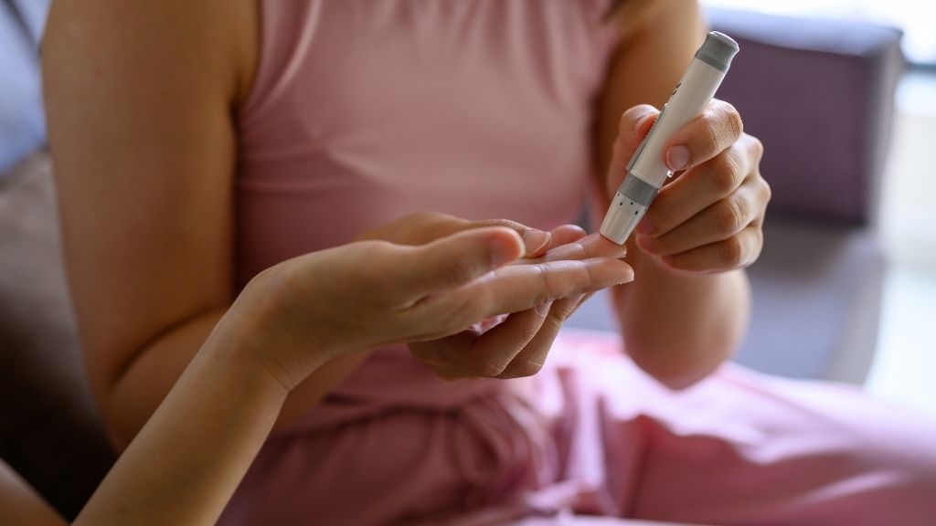 close up on two people&#039;s hands as one person helps the other take a blood glucose test