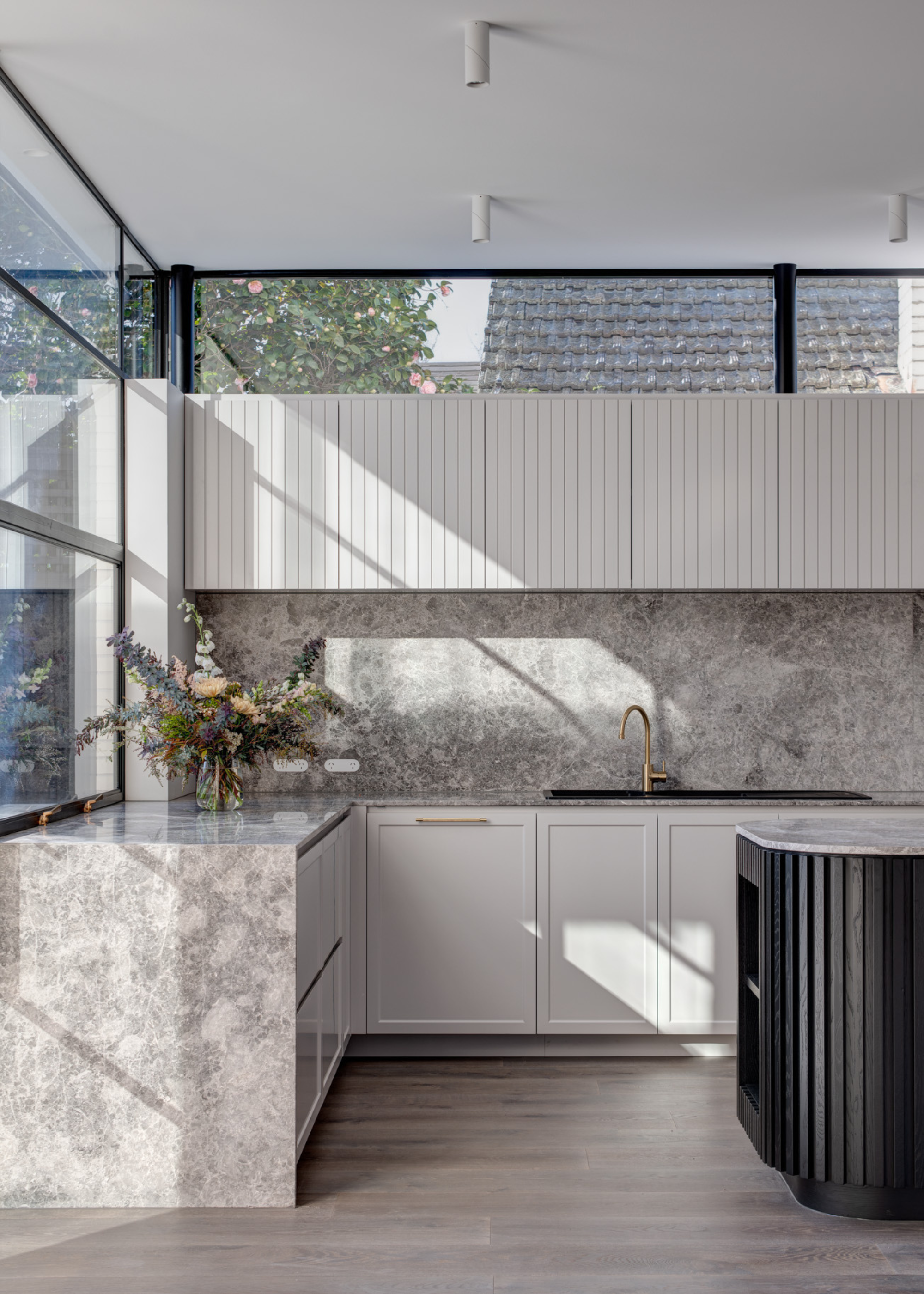 A kitchen with bright, airy gray stone countertops, white cabinets and a vase of flowers