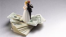 The bride and groom on a wedding topper stand back to back on top of a stack of cash.