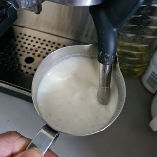 Silver jug filled with milk under a coffee machine milk steamer