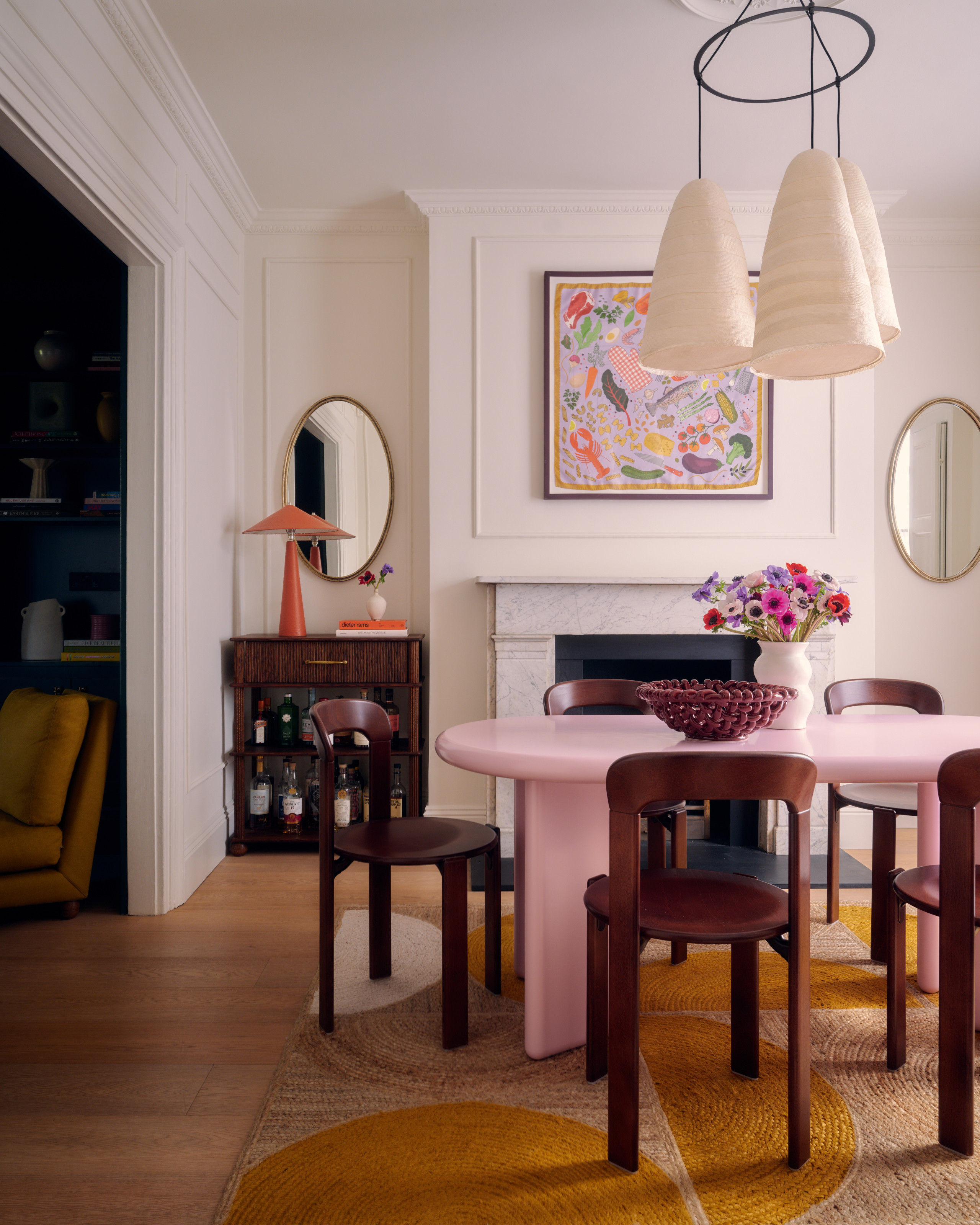 Dining room with pink lacquer table, brown wood chairs, three-pendant chandelier and pink and purple artwork