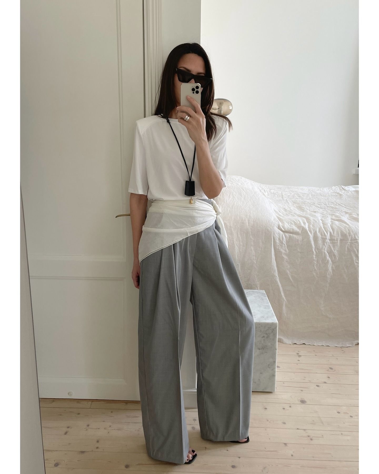 Woman in white t-shirt, gray pants and black pendant necklace