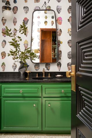 bathroom with green cabinet, retro wallpaper, retro mirror, black countertops, brass taps