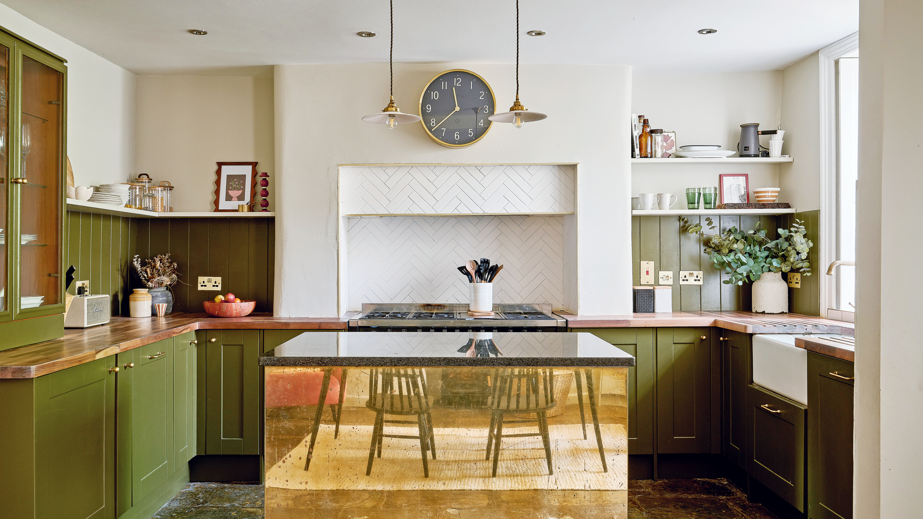 a green and white kitchen with a striking brass fronted kitchen island a Belfast sink, range cooker, white tiled splashback and slate flooring