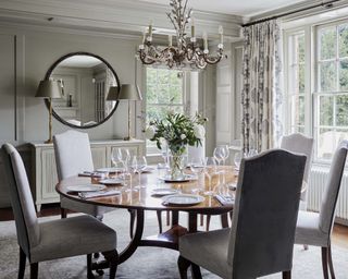 A dining room wall idea with dove grey paneled walls and a circular mirror over the fireplace