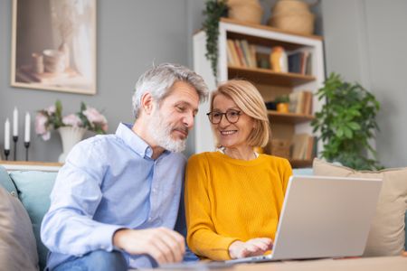 Mature couple relaxing on sofa, browsing internet on laptop together