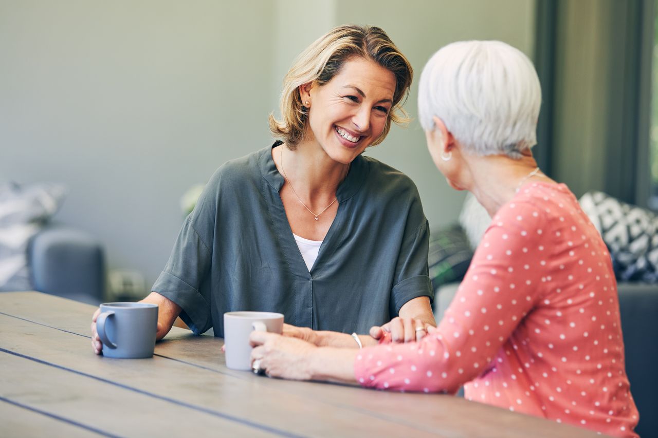 Two older women chatting holding mugs at a table