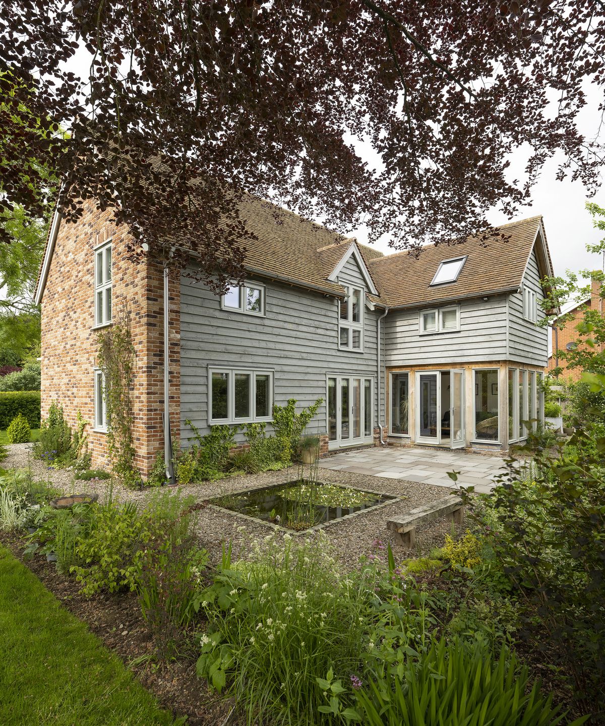 Exterior of a two storey oak frame house with brick and wood cladding with gravel garden and lush planting