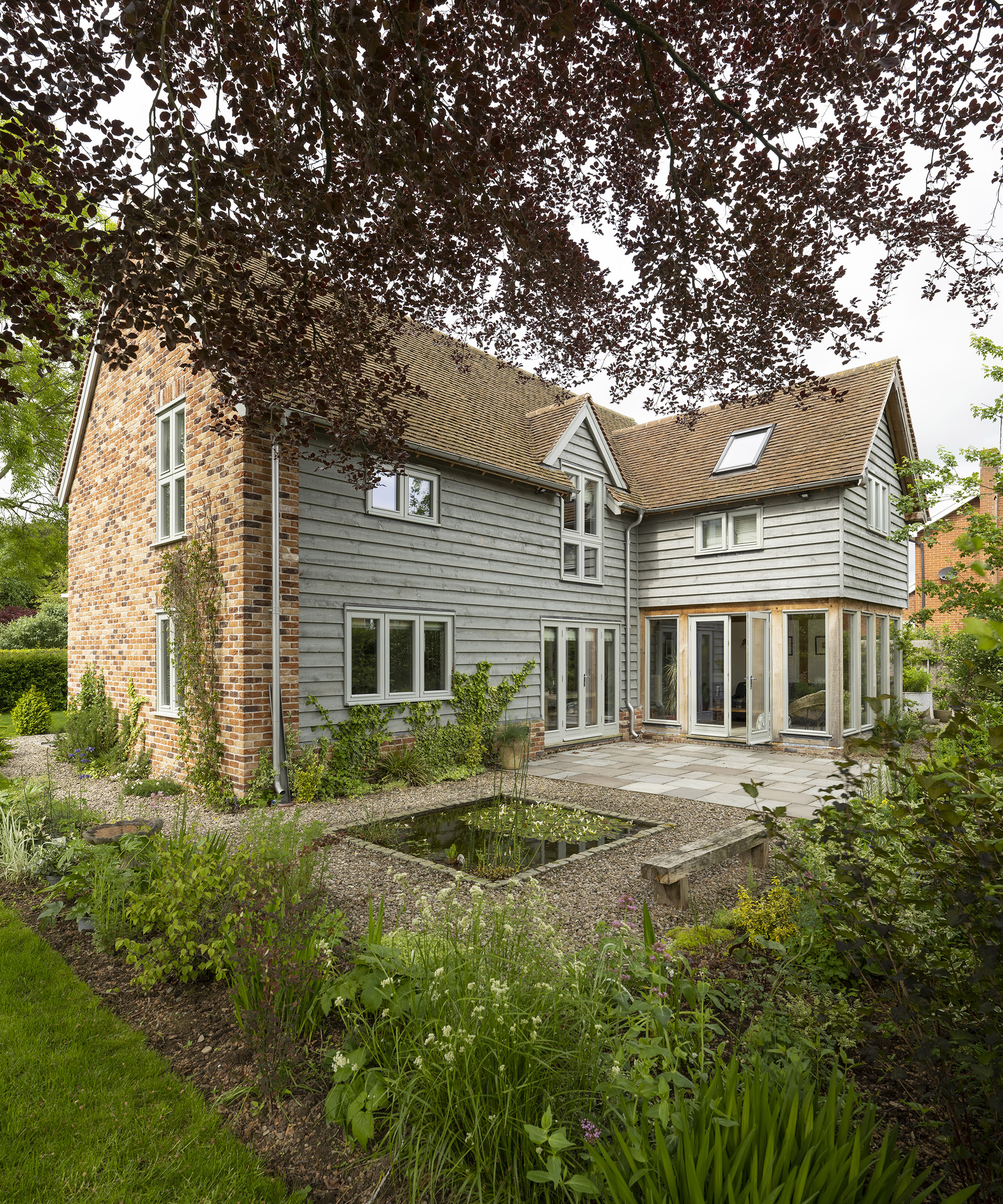 Exterior of a two storey oak frame house with brick and wood cladding with gravel garden and lush planting