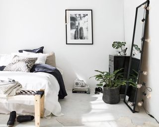 A monochrome bedroom with black framed mirror and string lights draped over it