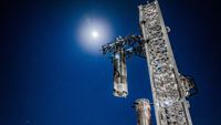 a large silver spacecraft is placed atop a booster by a launch tower at night