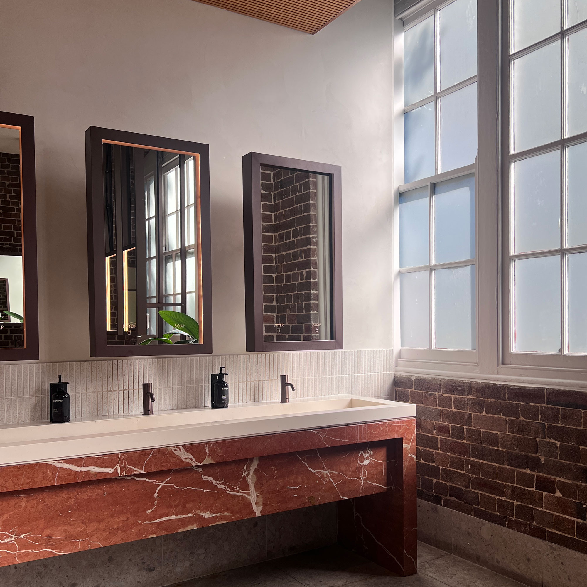 Bathroom with red marble countertop, long sink and three rectangular mirrors