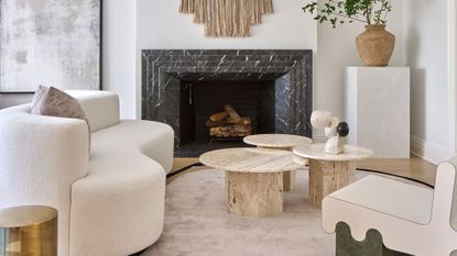 minimalist neutral living room with white boucle sofa, marble coffee table and black marble fireplace