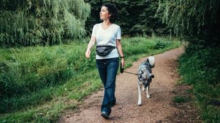 Woman walking dog through trail paths, wearing jeans and top