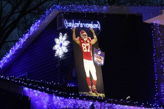 A house covered in Christmas lights and an image of Travis Kelce in his Chiefs uniform that says Taylor's Version