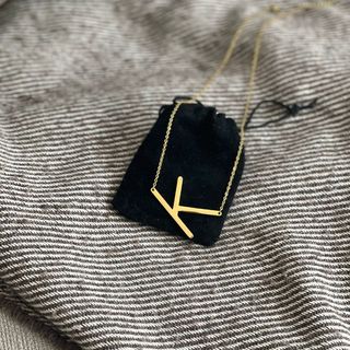 A sideways gold 'K' initial necklace laying against a small black velvet bag