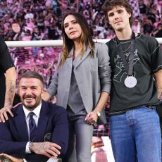 Victoria Beckham stands alongside David Beckham wearing a grey three-piece suit with skinny trousers and black peep-toe shoes.