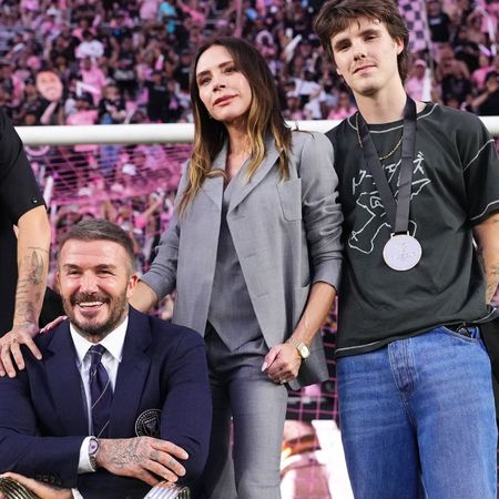 Victoria Beckham stands alongside David Beckham wearing a grey three-piece suit with skinny trousers and black peep-toe shoes.