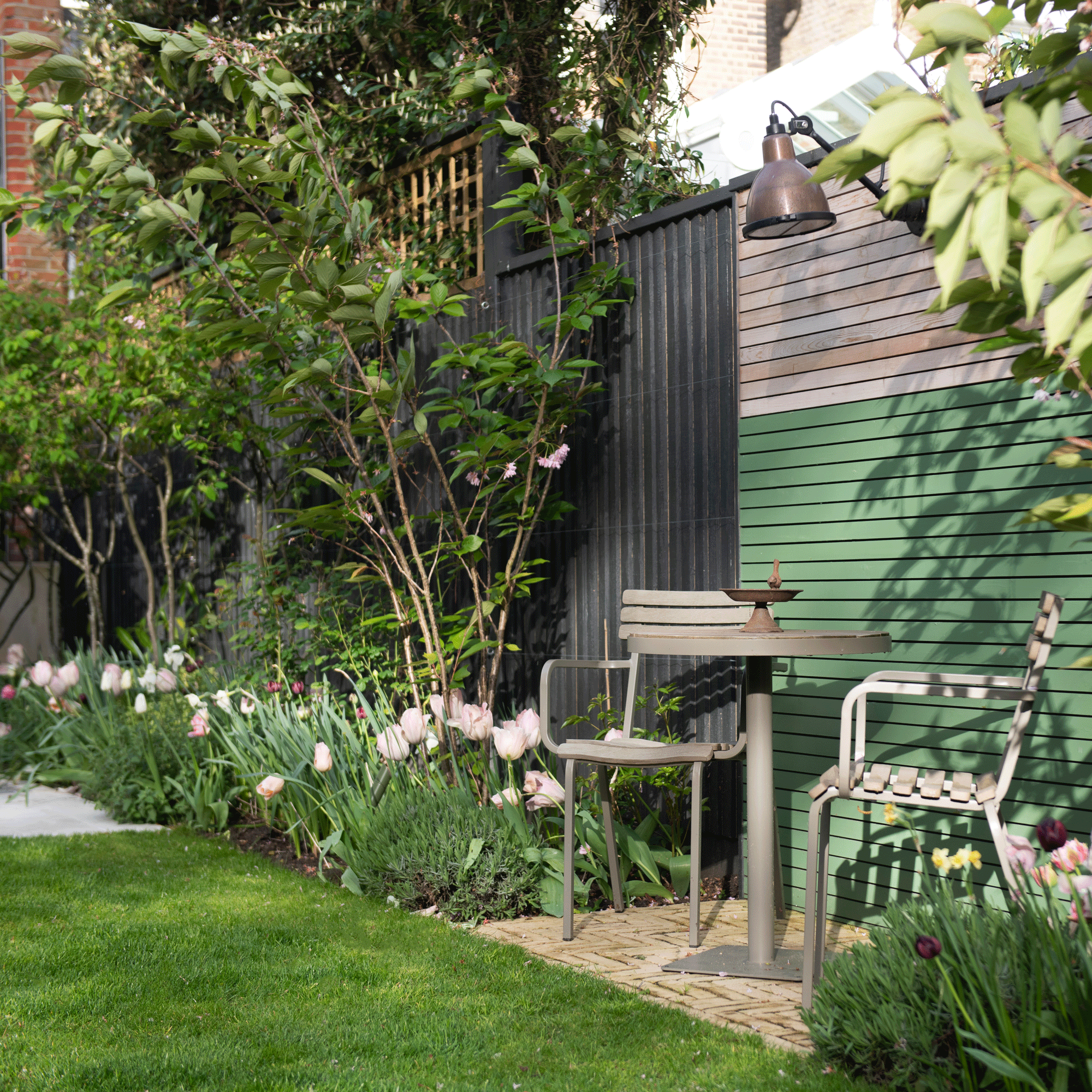a garden with a bistro set in front of a two tone painted fence and a lawn with lots of tulips