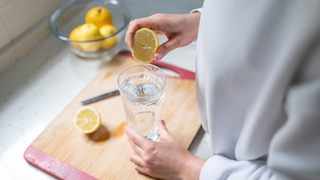 A person squeezing a lemon into a glass of clear liquid