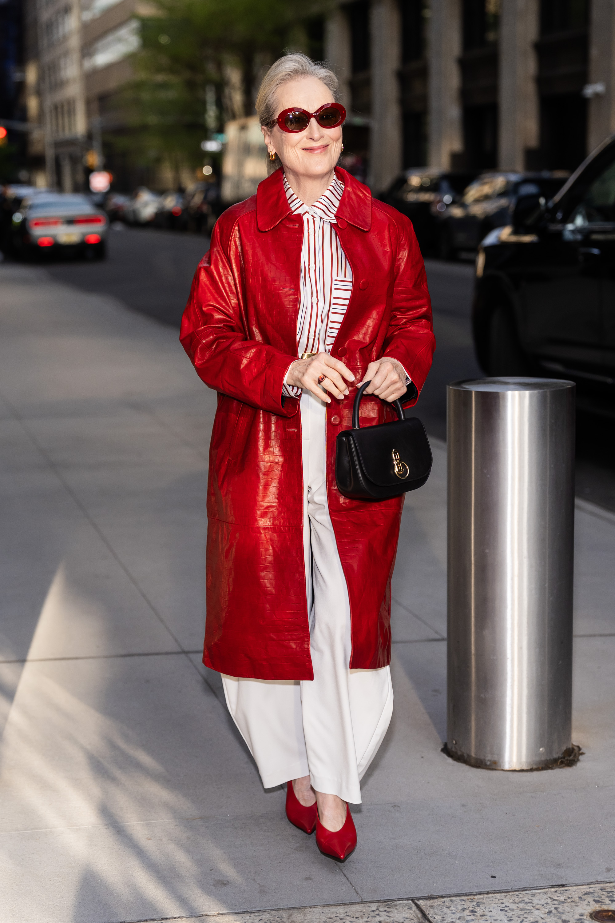 Meryl Streep steps outside in New York wearing a red leather coat with white jeans and red pointed-toe shoes and red sunglasses.