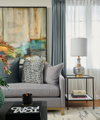 End of gray sofa styled over a rug with an end table and Tom Ford Coffee Table Book