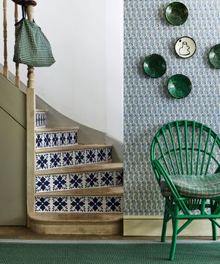 Hallway, wooden staircase with Mediterranean tile wallpaper pattern on risers, green wicker chair, green wall mounted ceramic plates. Floral printed wallpaper and floor carpet runner.