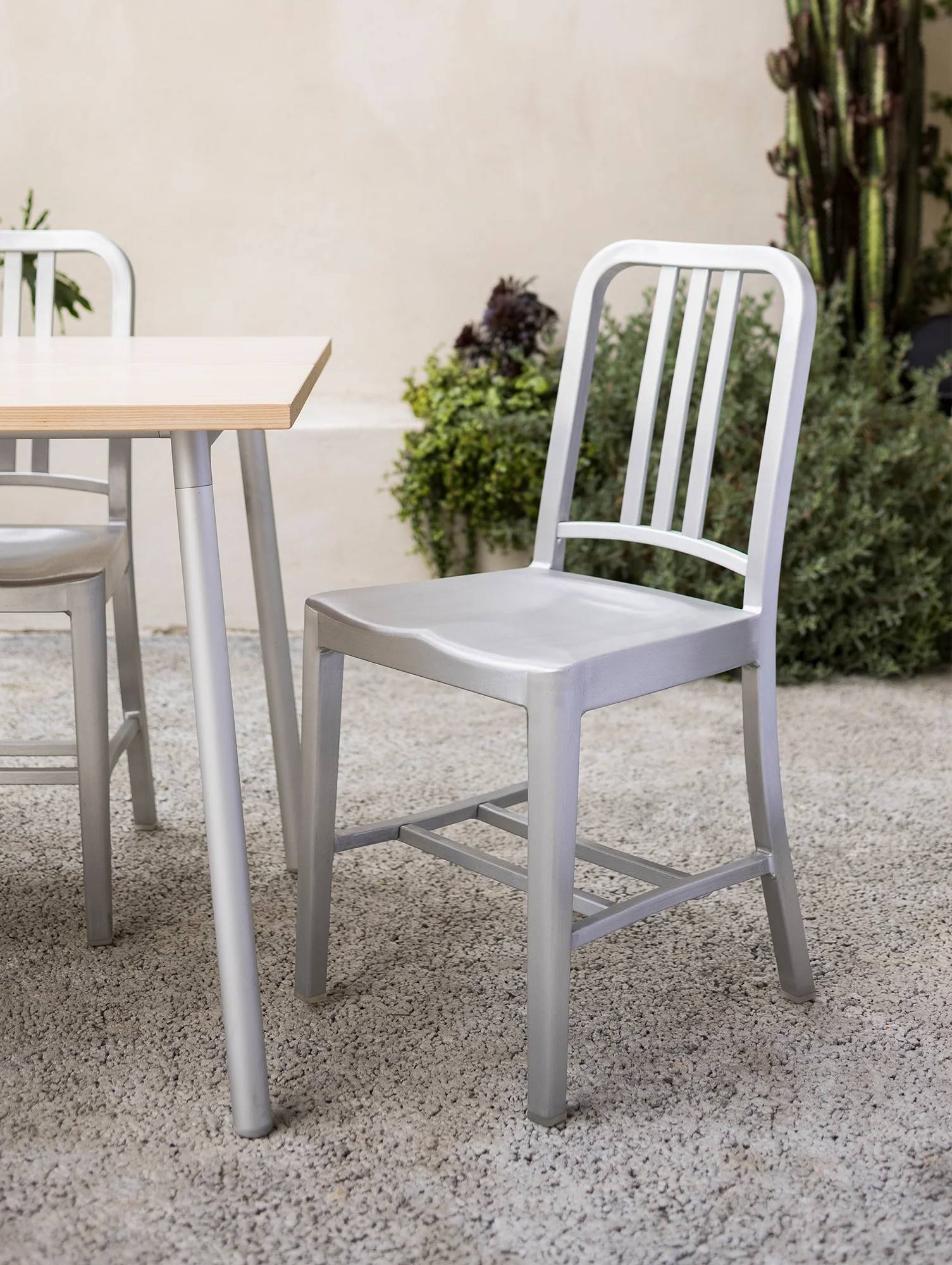 metal chair and table on gravel with plants in the background
