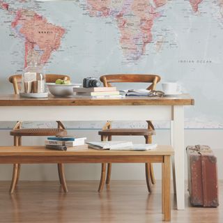 small dining room with map mural, bench seating with two chairs, suitcase, maps, tableware