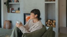 Woman sitting in cosy home in autumn holding cup of herbal tea and looking away from the camera, representing when do the clocks go back