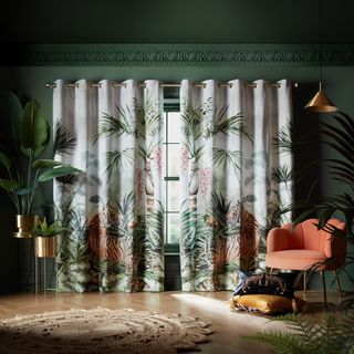 Botanical curtains hanging in a dark green walled room with wooden flooring and a peach armchair