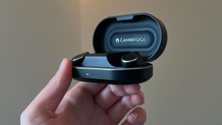 Reviewer hand holding Cambridge Audio M100 earbuds in charging case