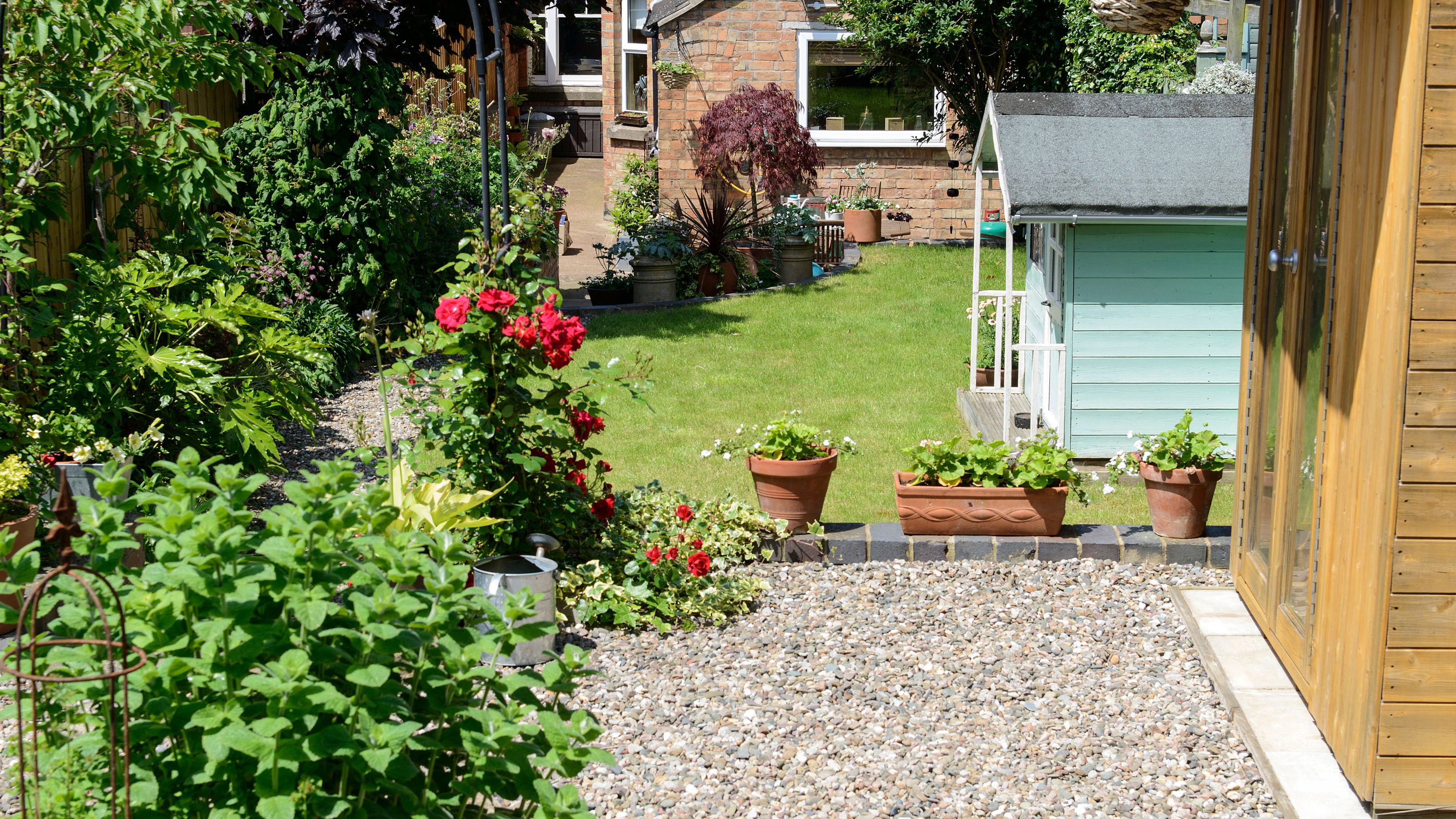 Gravel garden in front of grass lawn with potted plants and Wendy house