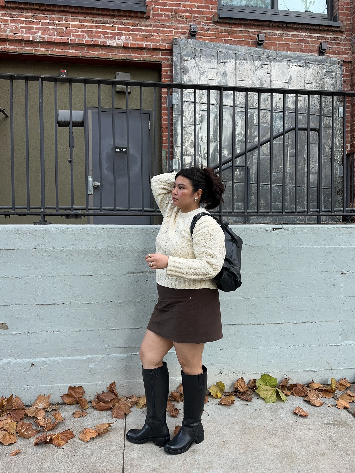 Influencer @marina_torres wears a brown miniskirt with black knee-high boots and a cream knit.