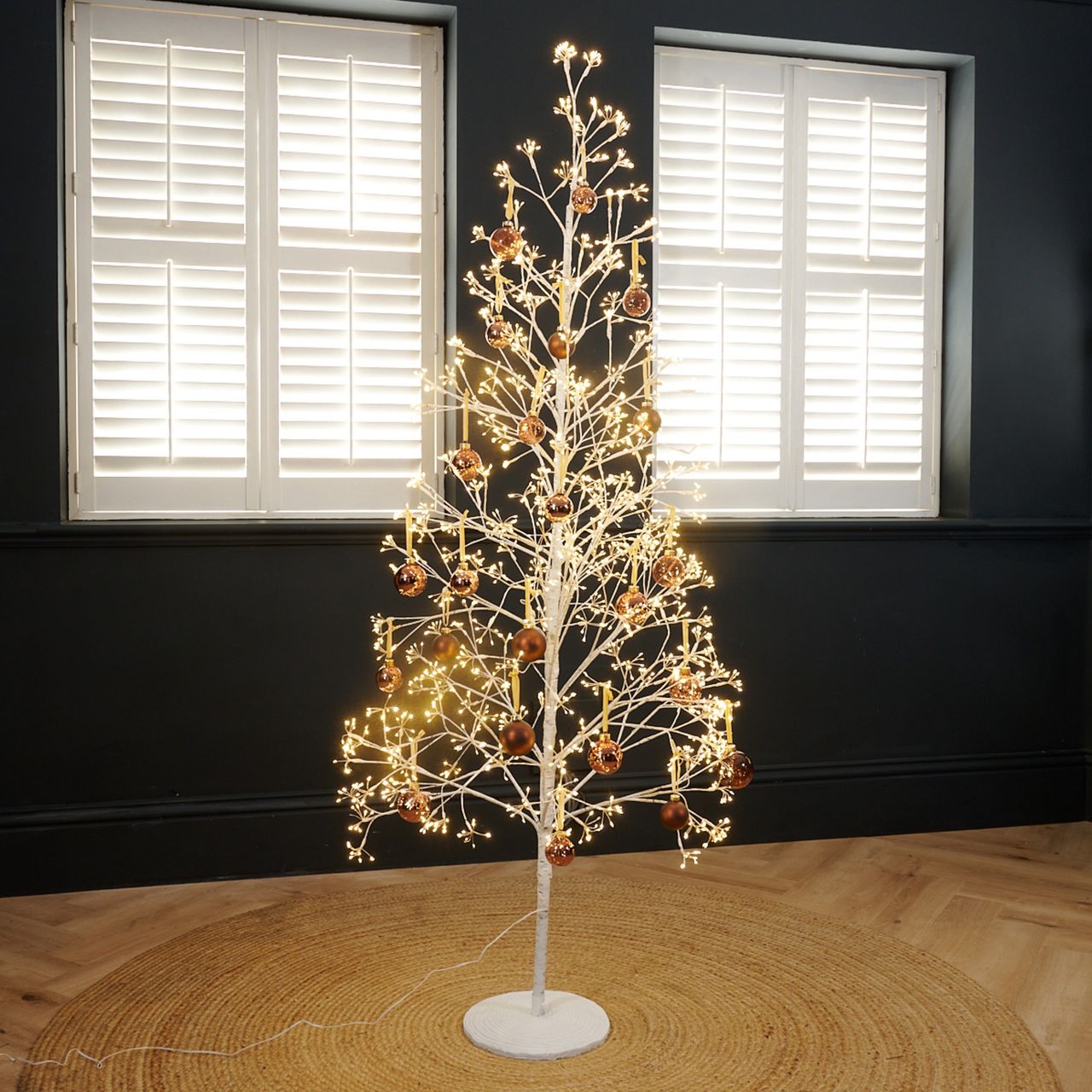Next's White Twig 6ft Pre Lit Christmas Tree decorated with brown baubles set up in a black-painted living room