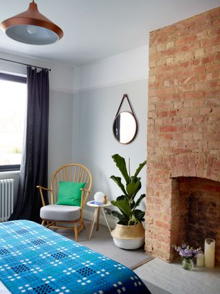 bedroom with a mid-century chair in the corner, exposed brick fire place and a plant