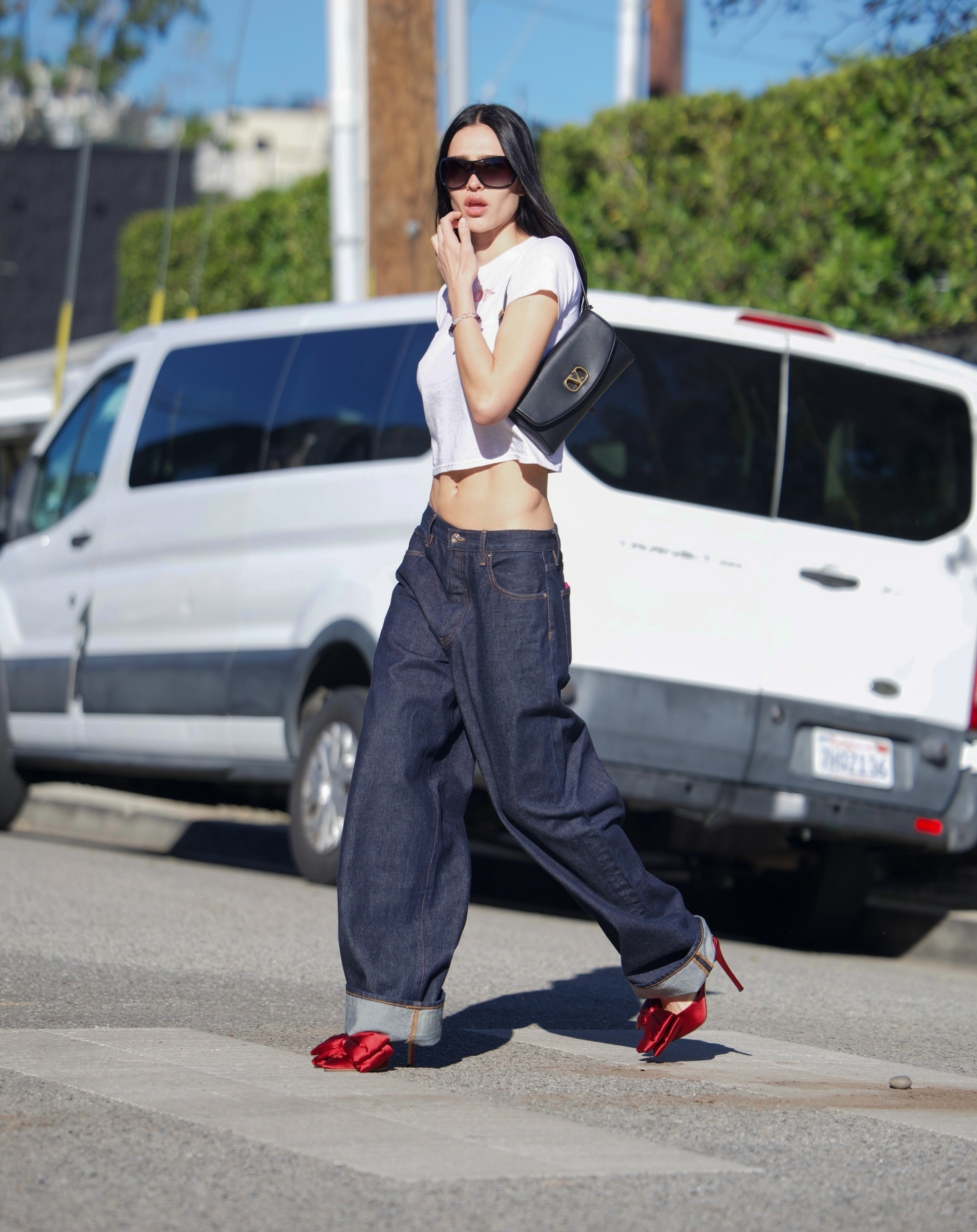Amelia gray wears a white tee, black valentino bag, baggy jeans, and red heels with a bow.
