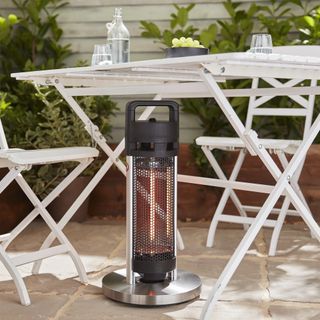 A small electric patio heater in front of a white bistro set